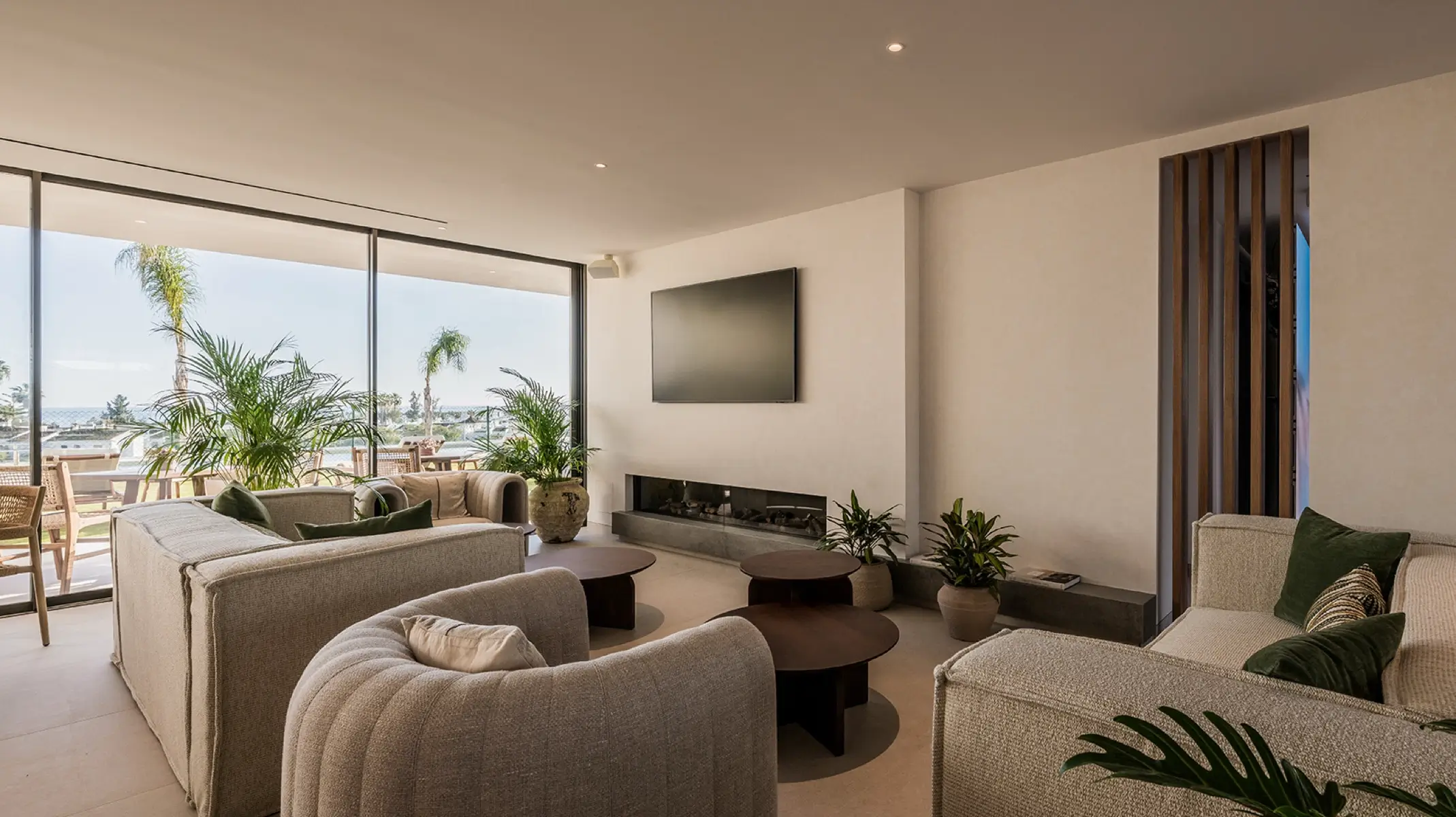 Gemeinschaftslounge bei Naghoi — bodentiefe Fenster mit Meerblick, Kamin und bequeme Sitzbereiche, Einrichtung zur postoperativen Erholung in Marbella.