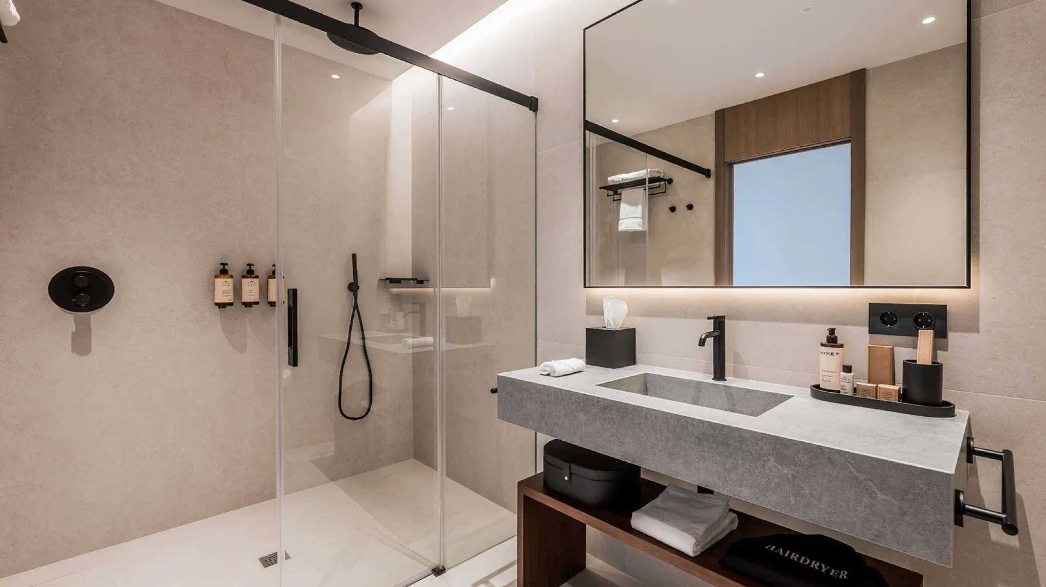 Gästebad von Naghoi — hochwertige Steinoberflächen, Glasdusche und luxuriöse Nuxe-Produkte in einem postoperativen Erholungszimmer in Marbella.